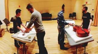 The JACK Quartet rehearsing with tied together string instruments on tables.